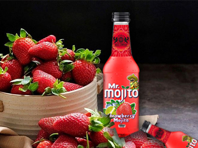 A bowl of fresh strawberries next to a bottle of mr. mojito strawberry mojito on a dark background.